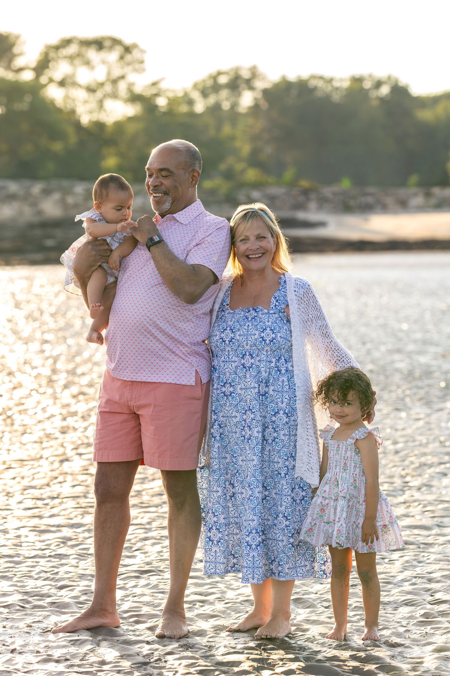 Happy family of four posing on a sunny beach, grandparents holding two young grandchildren near the water.