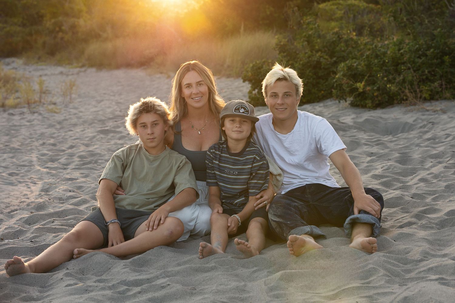 Family members relaxing together on a sandy beach at sunset with golden light glowing in the background.