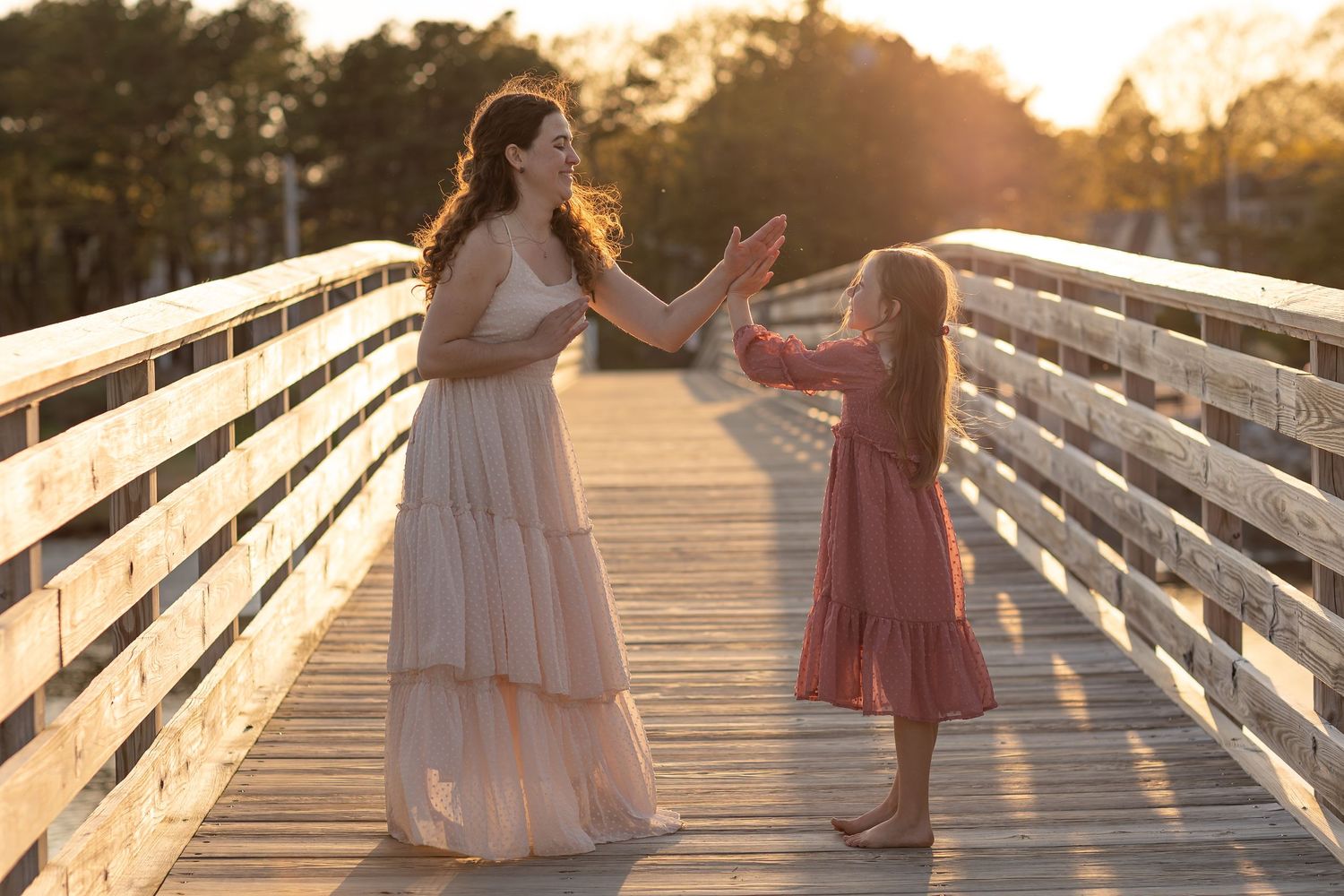A parent and child walk together on a wooden boardwalk during sunset.