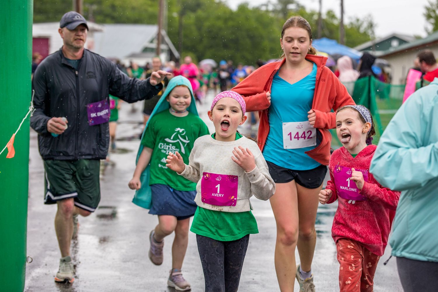 Children and adults cross the finish line together during a fun run race event on a rainy day.