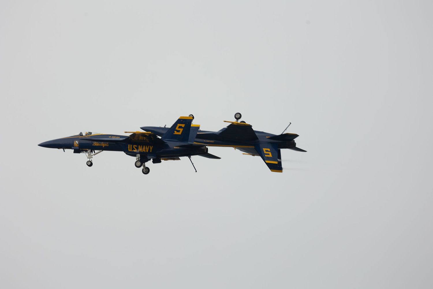 Military jets perform aerial maneuvers with contrails against a cloudy sky.