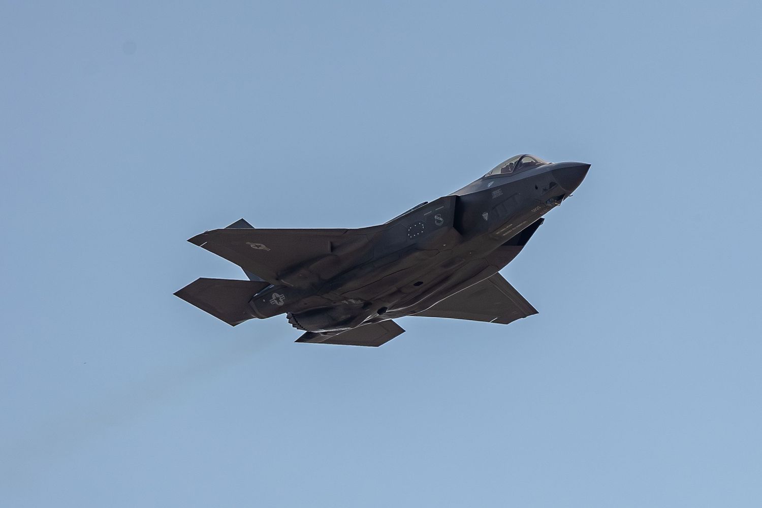 F-35 Lightning II stealth fighter jet flying against blue sky during aerial demonstration.