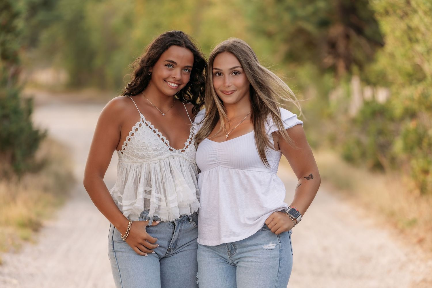 Two friends in casual summer outfits posing on dirt path with natural backdrop.