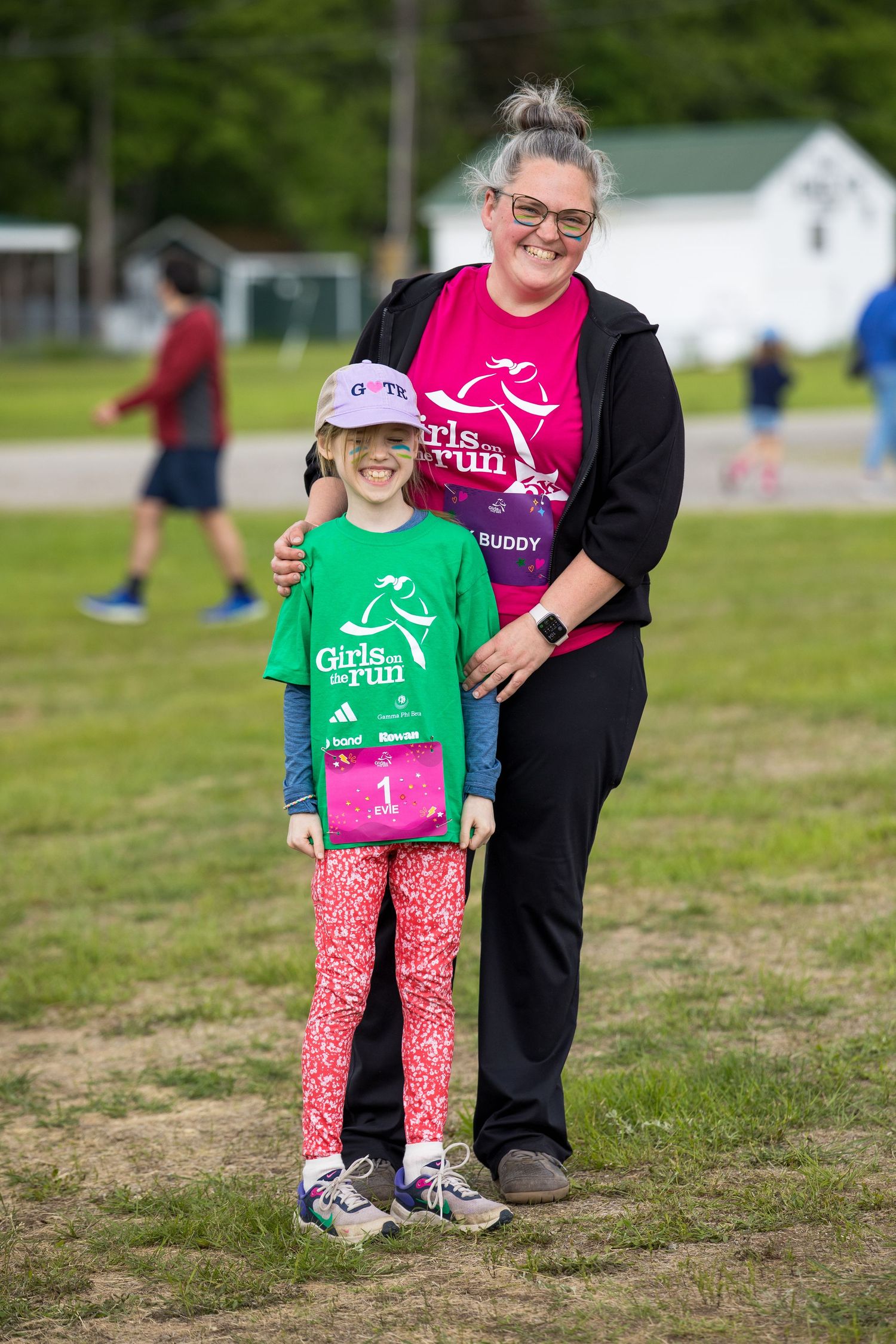 A girl and woman in Girls on the Run shirts pose together smiling at an outdoor 5K race event.