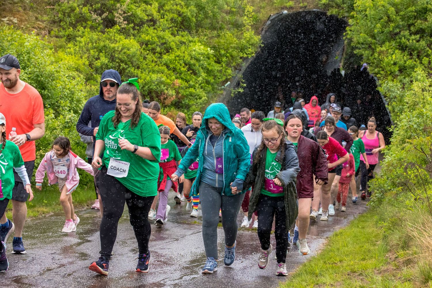 Participants walking and jogging on a muddy trail during a charity fun run event on a rainy day.