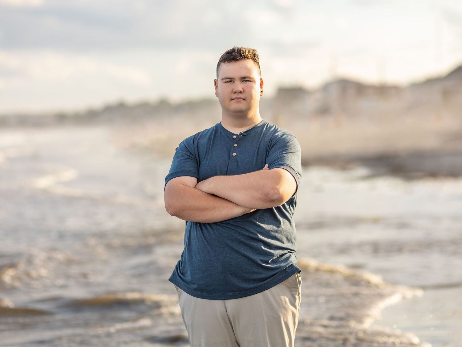 Person walking along a sandy beach at sunset with waves crashing in the background.
