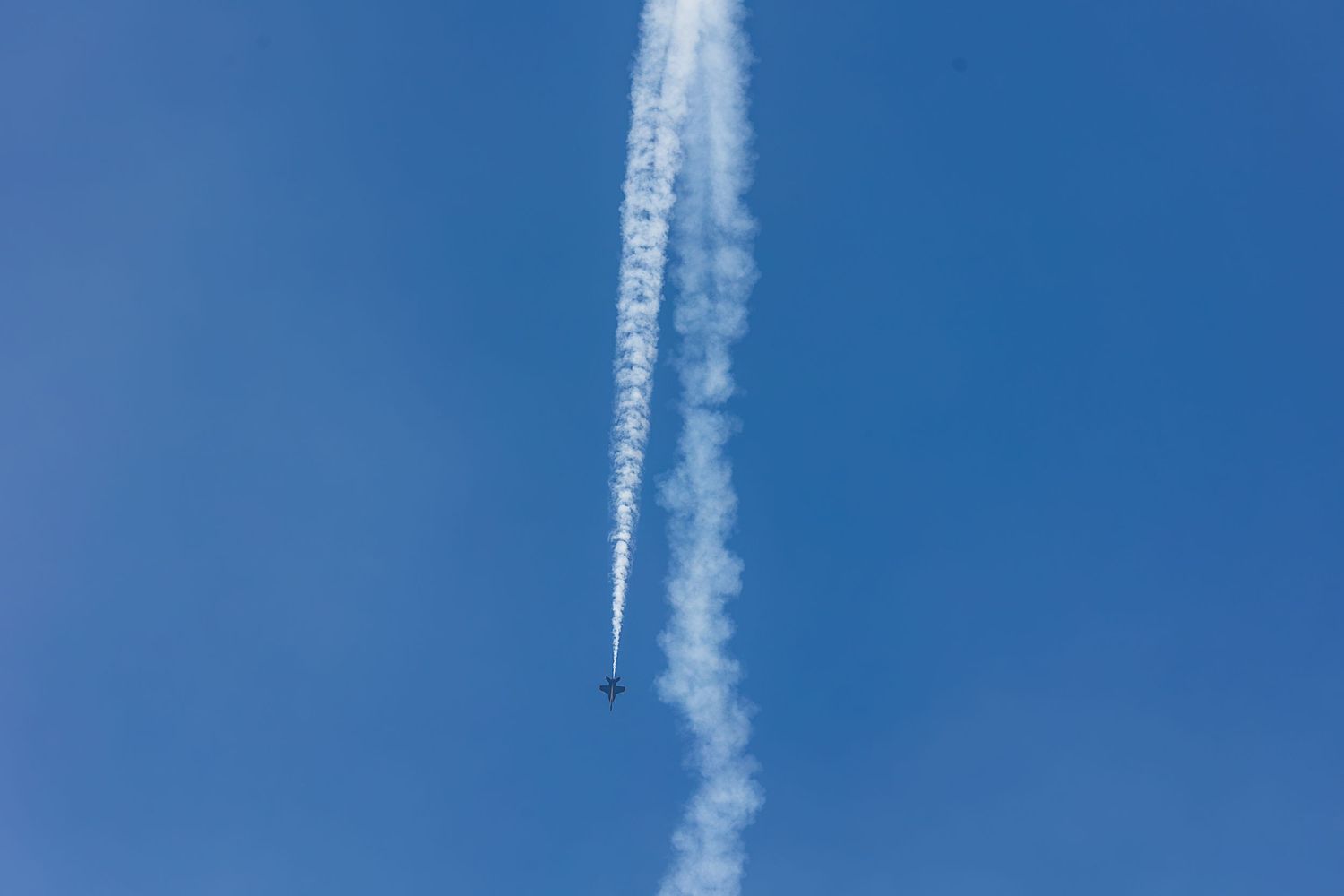 Five white contrails streak across a bright blue sky creating parallel lines in a clear daytime atmosphere.