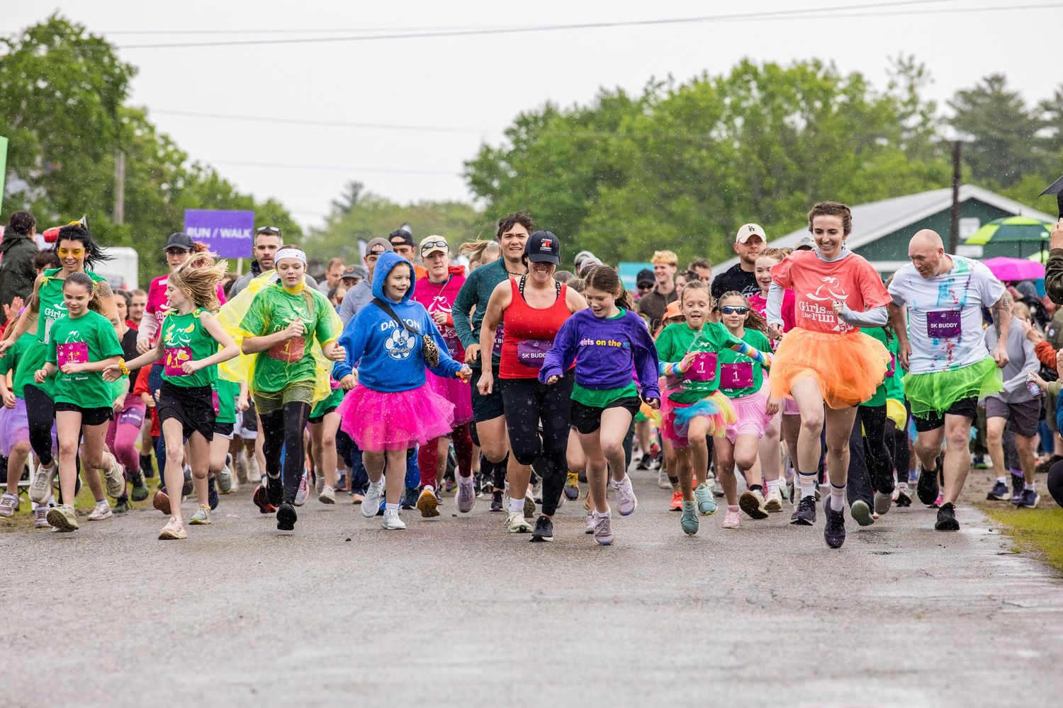 Colorful fun run participants in bright costumes race together at the start of an outdoor charity 5K event.