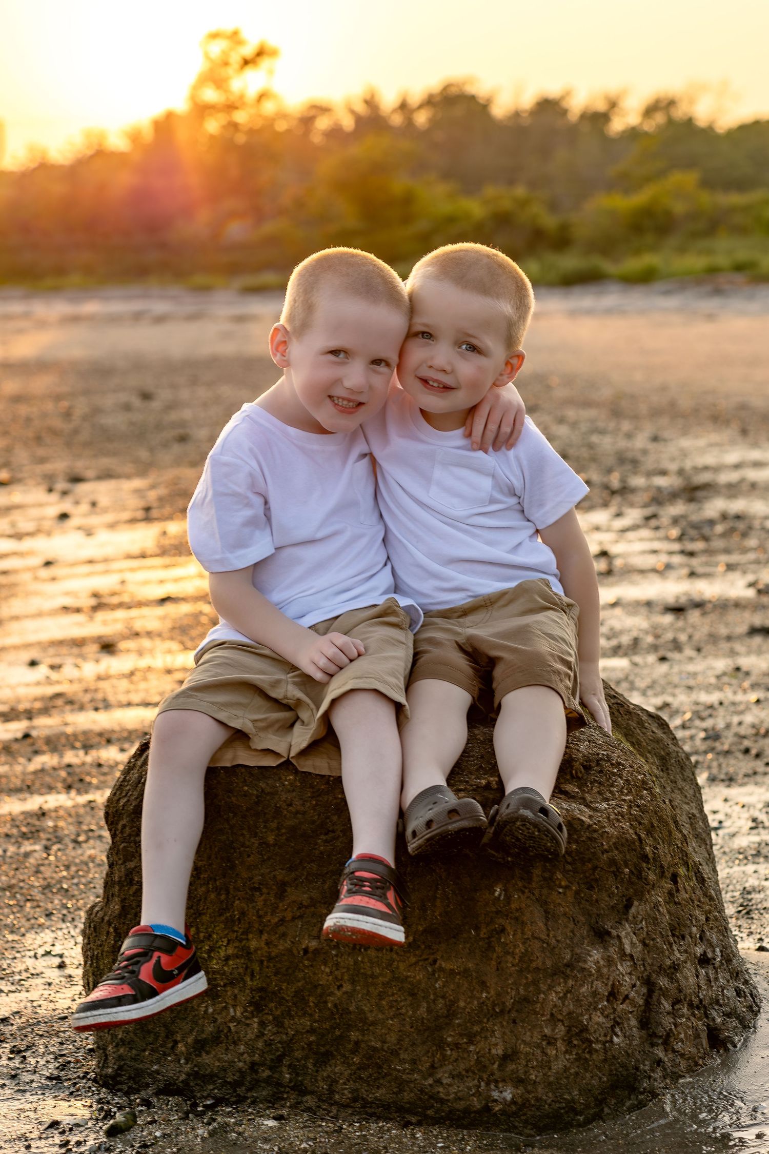 Two children in white shirts sitting together on a rock at sunset.