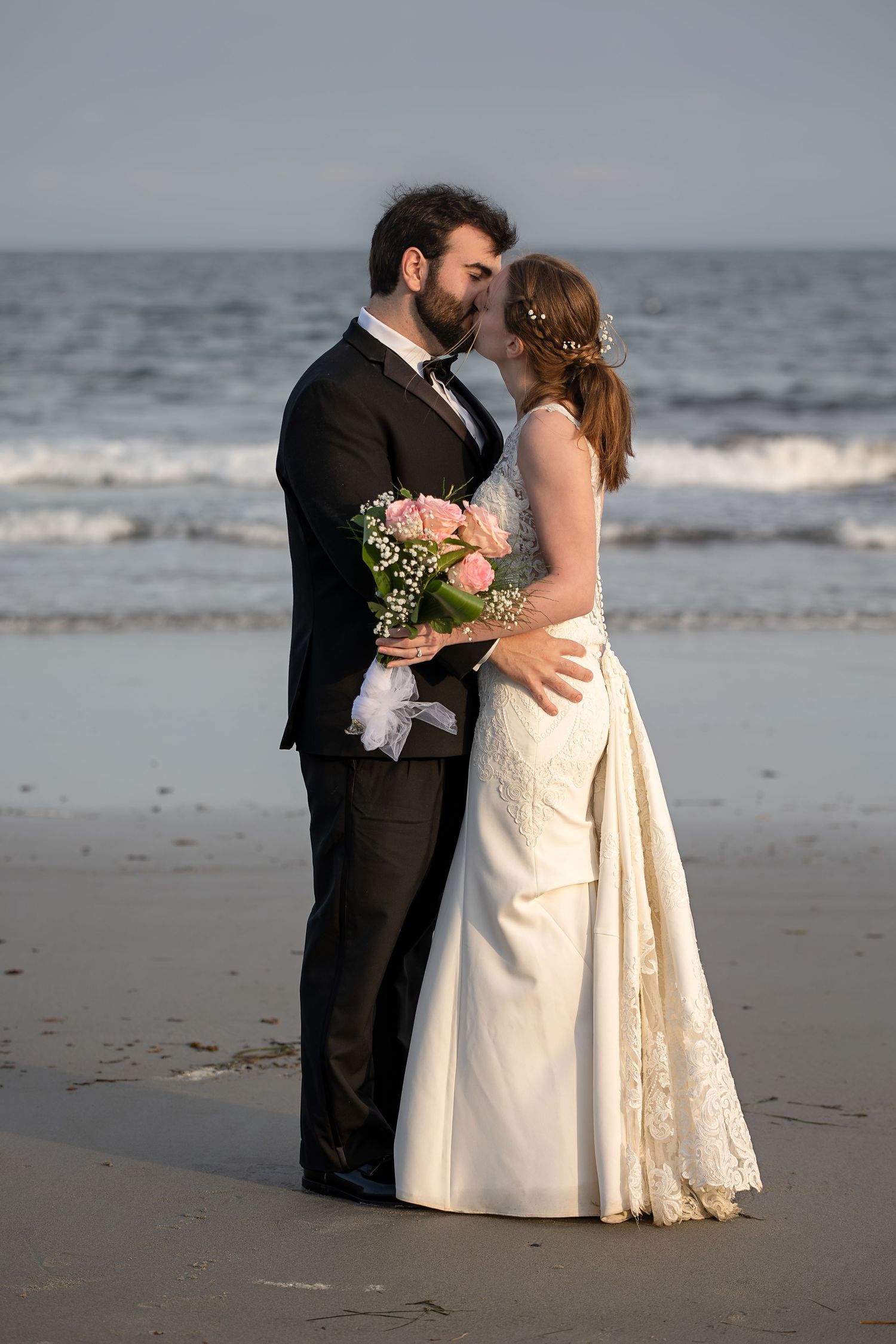 A couple in wedding attire dances romantically on Mother's Beach in Kennebunk, Maine at sunset.