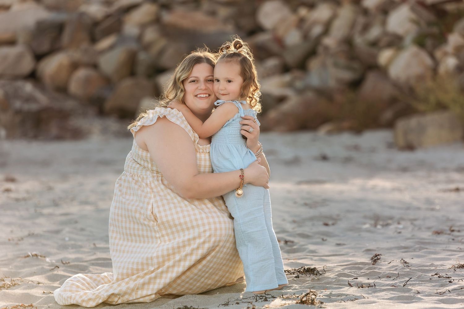 A tender beach portrait showing embrace against rocky shoreline at sunset.