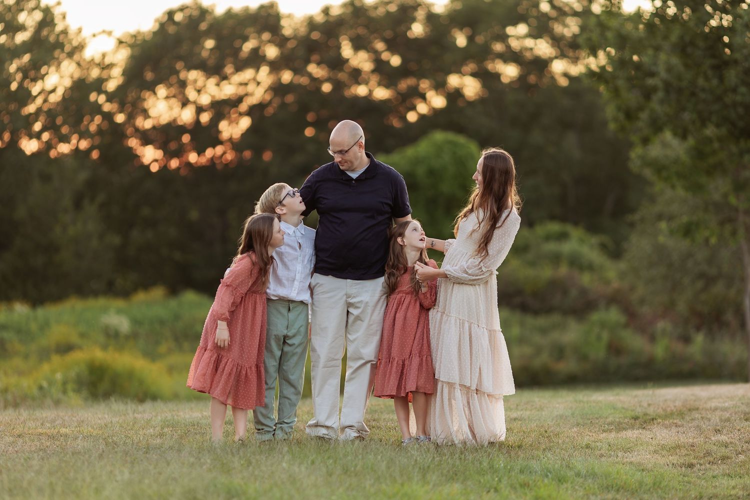 A group in coordinating outfits walks together in a grassy field during golden hour sunset.