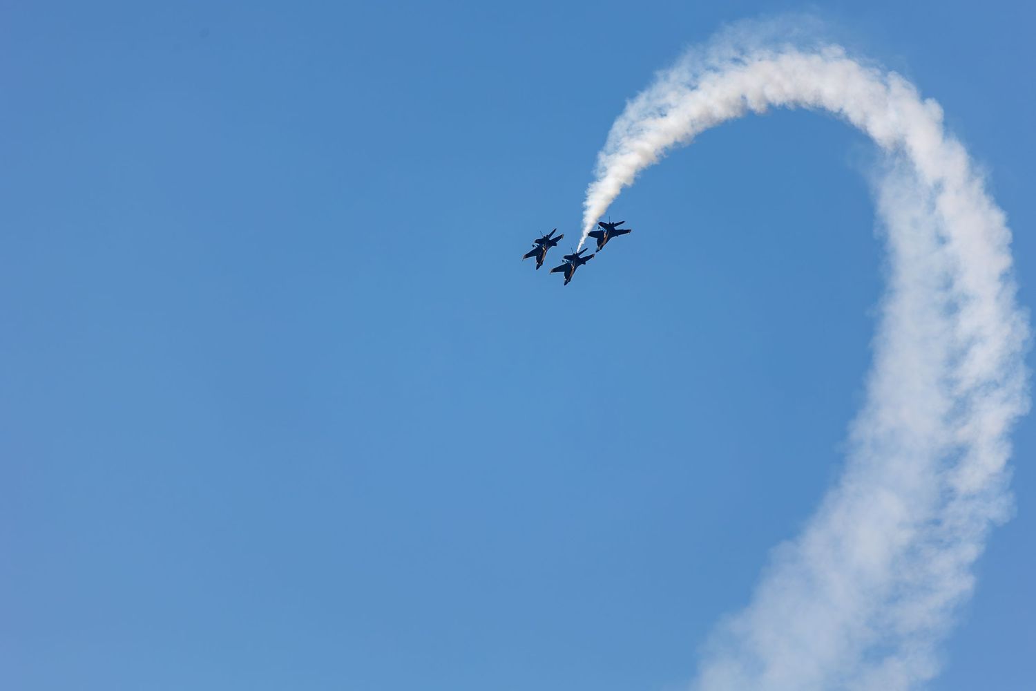 Two military jets perform a synchronized loop maneuver at an airshow, leaving a white smoke trail against a clear blue sky.