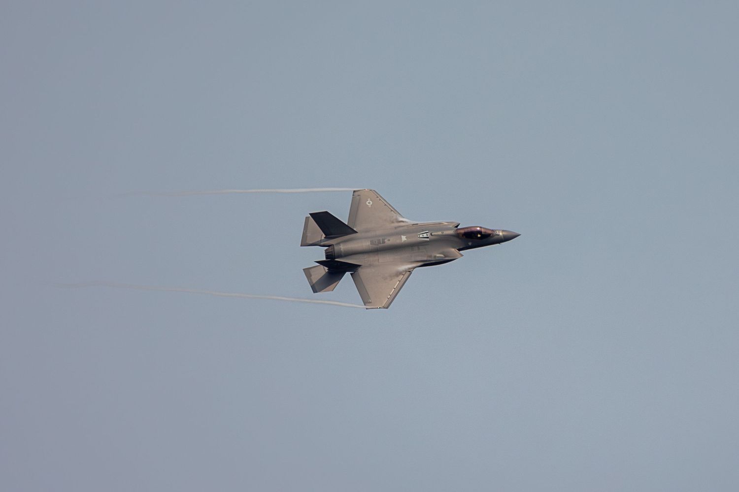 A sleek F-35 stealth fighter jet flying at high speed during an airshow demonstration against a gray sky.