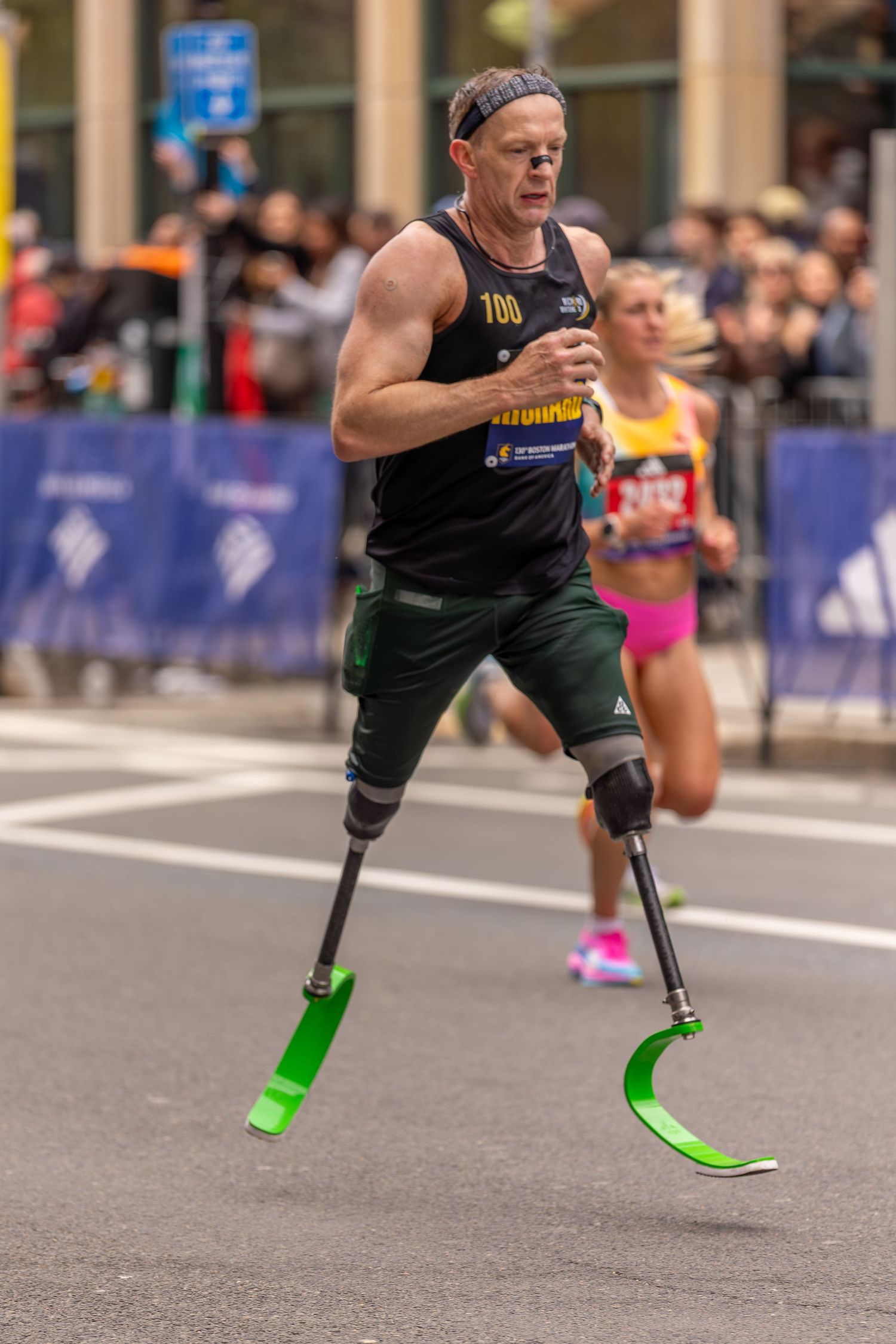 Determined double amputee athlete races on blade prosthetics in a marathon, wearing bib number 100.