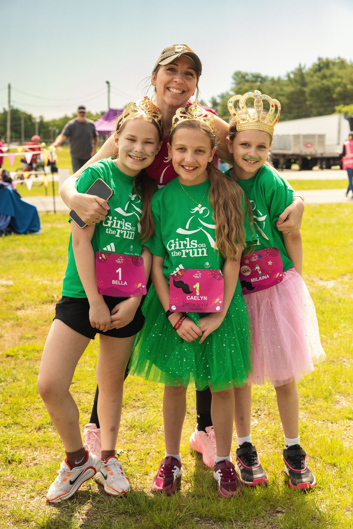 Woman and three girls in green Girls on the Run shirts and gold crowns pose after a race.