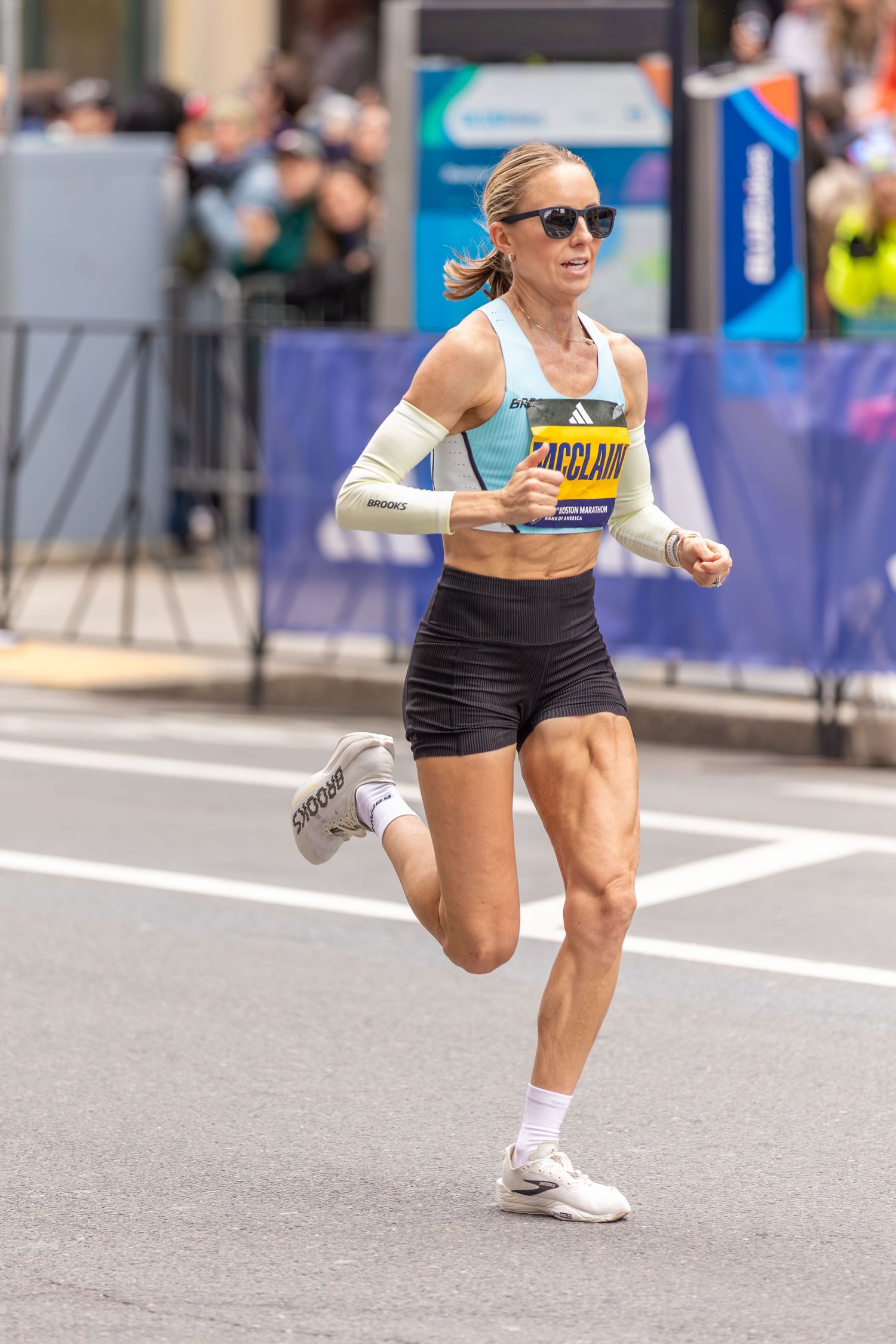 Female runner McClain in light blue top and black shorts racing at the Boston Marathon.