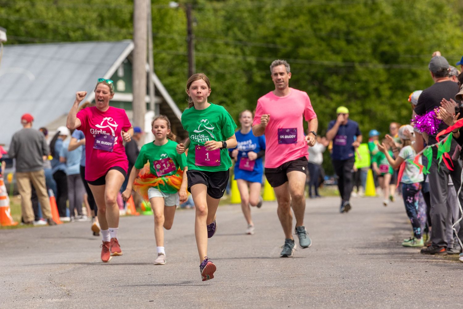 Runners of all ages sprint toward the finish line at an outdoor 5K charity race on a sunny day.