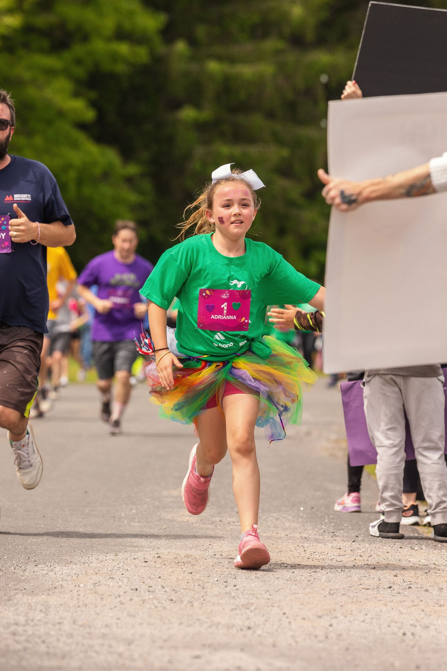 Young girl in green shirt and rainbow tutu runs energetically in a fun color run race event outdoors.