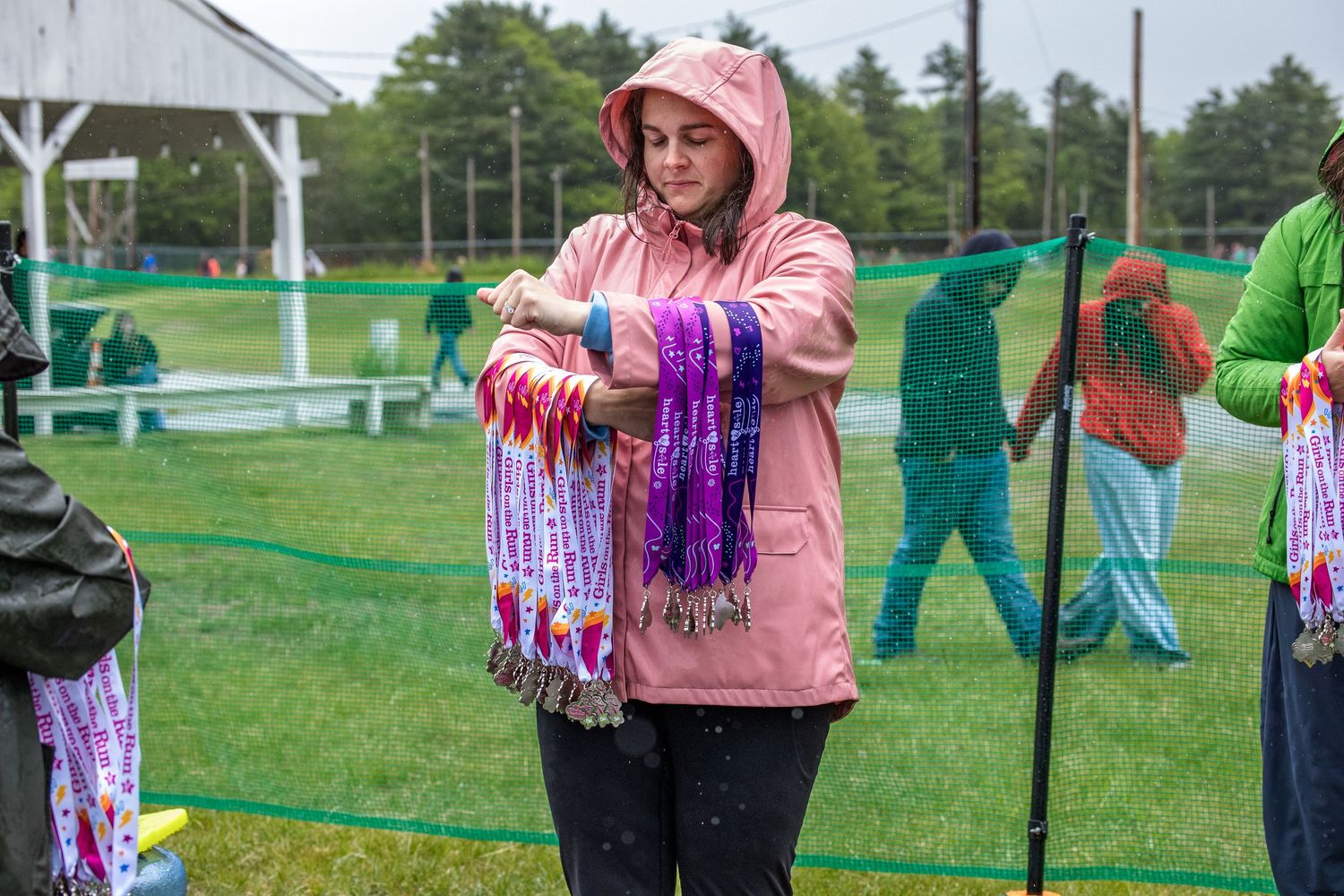 Woman in pink raincoat holding colorful ribbons at an outdoor event on a rainy day.