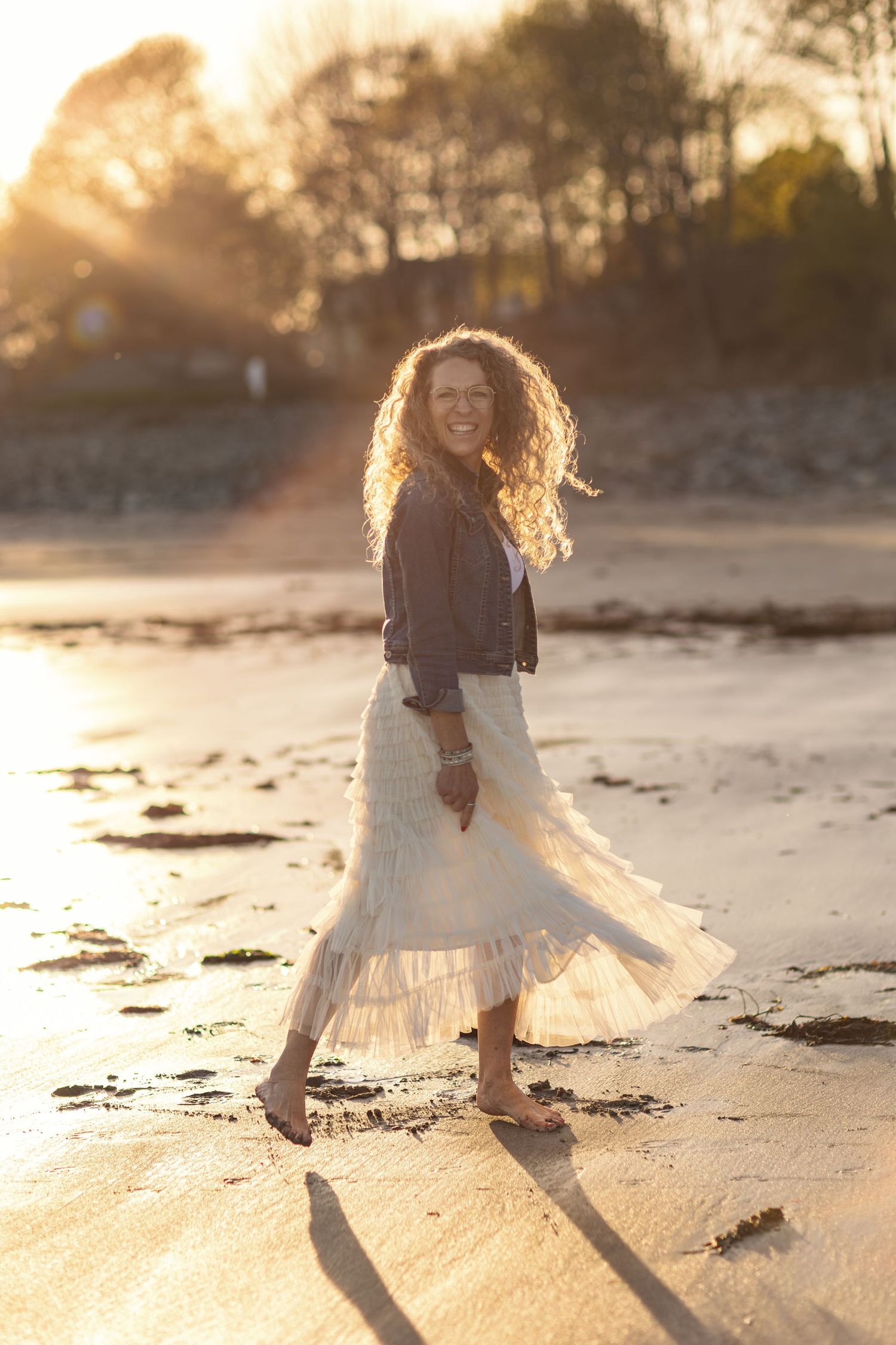 A child in a white dress twirls on the beach at sunset.