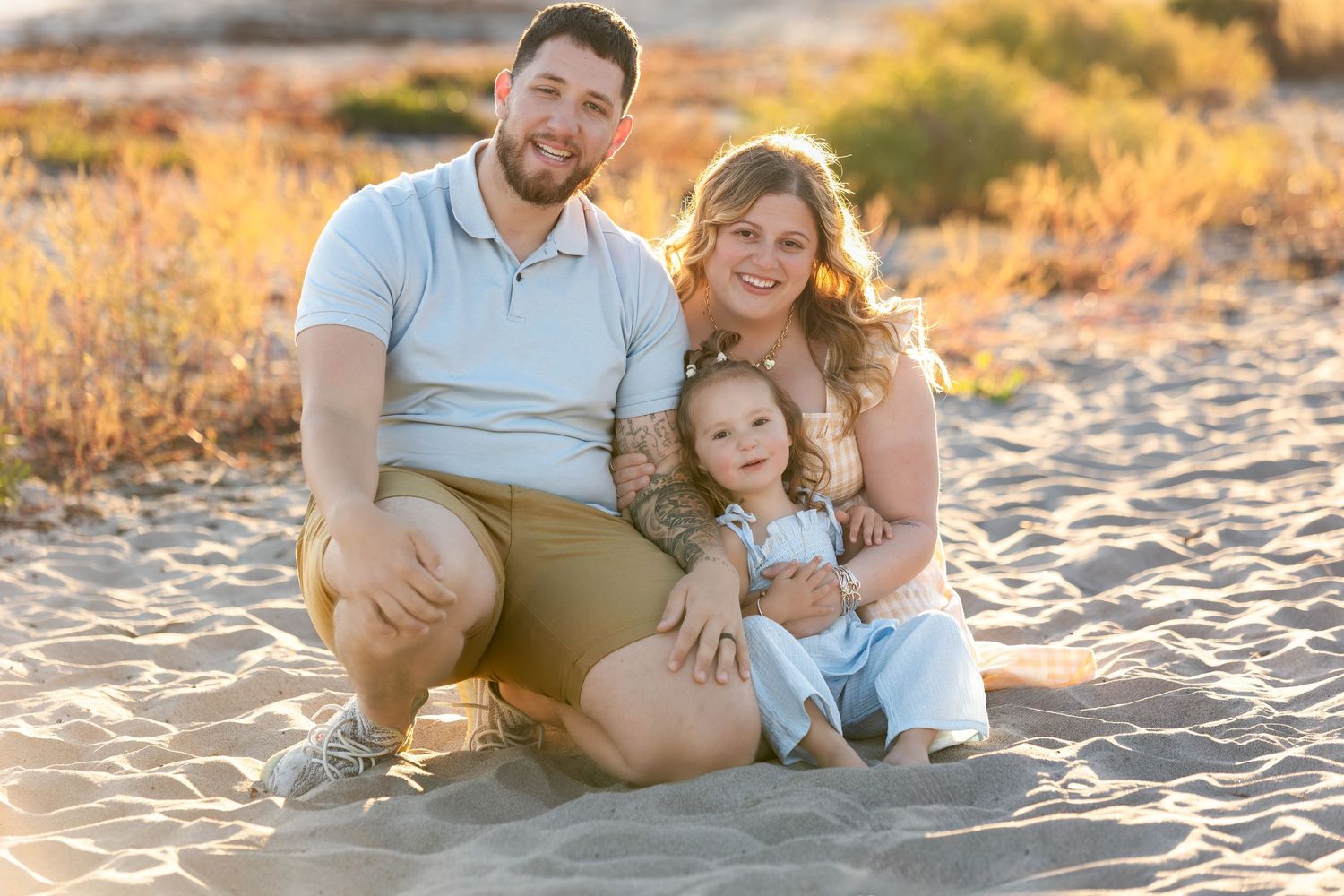 A family sits together on a sandy beach at sunset during a warm golden hour photo session.