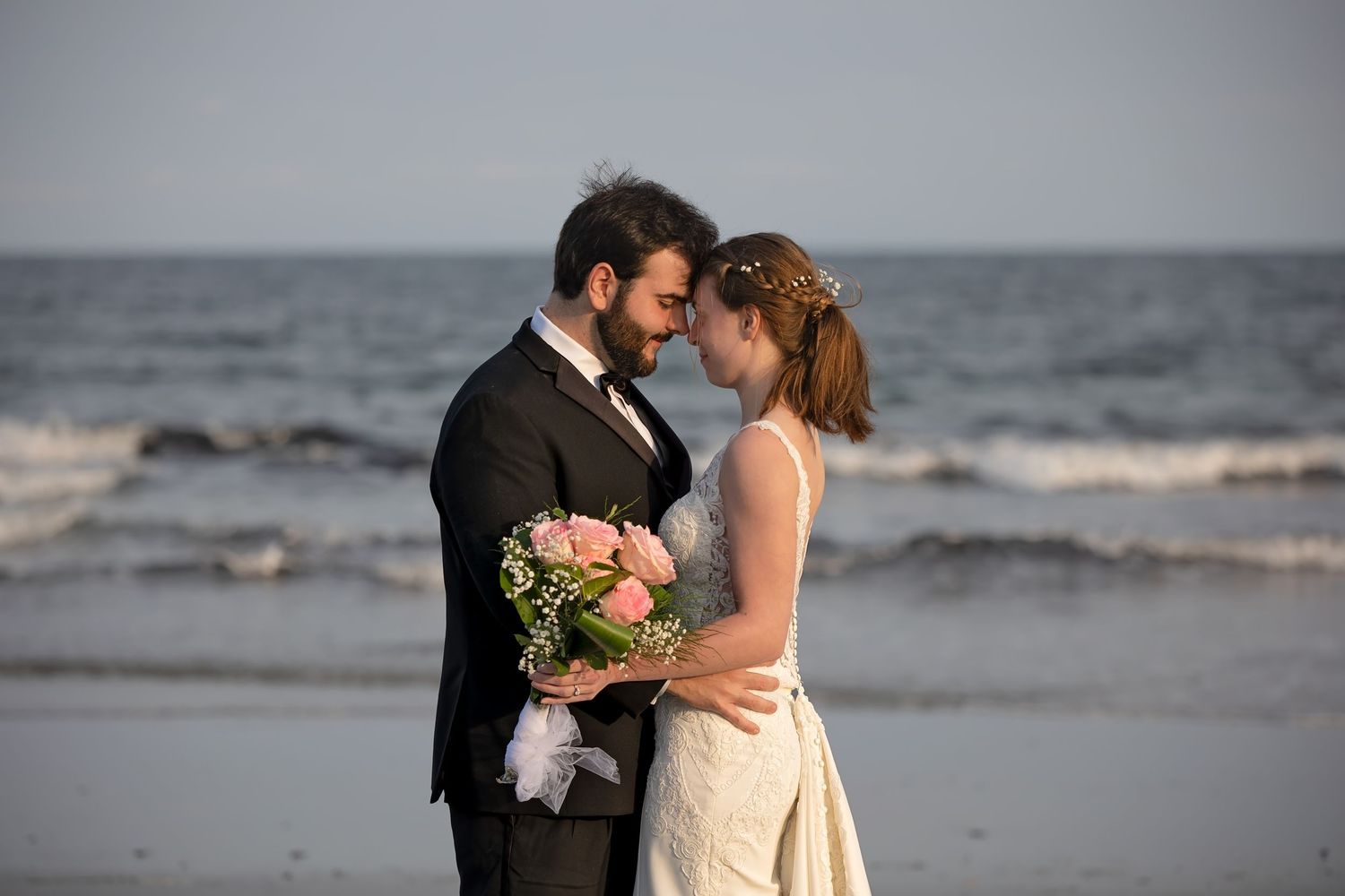 A couple in wedding attire dances romantically on Mother's Beach in Kennebunk, Maine at sunset.