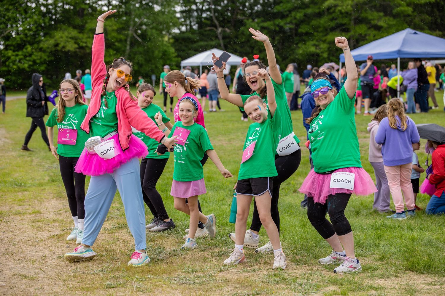 Group of women in green and pink tutus celebrating at a charity fun run event on a grassy field.