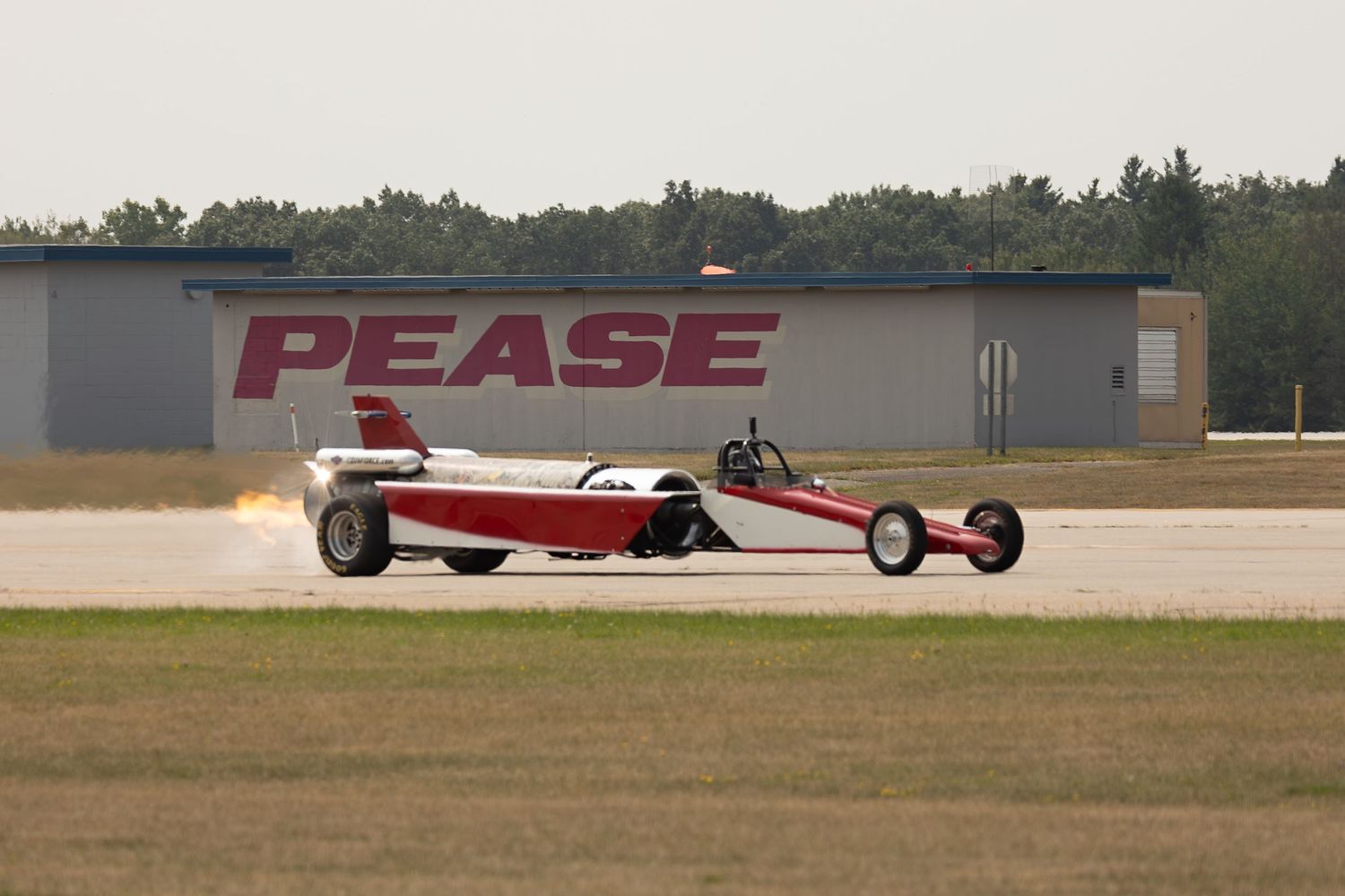 A red vintage drag racing car speeds along a dirt track during a motorsport competition event.