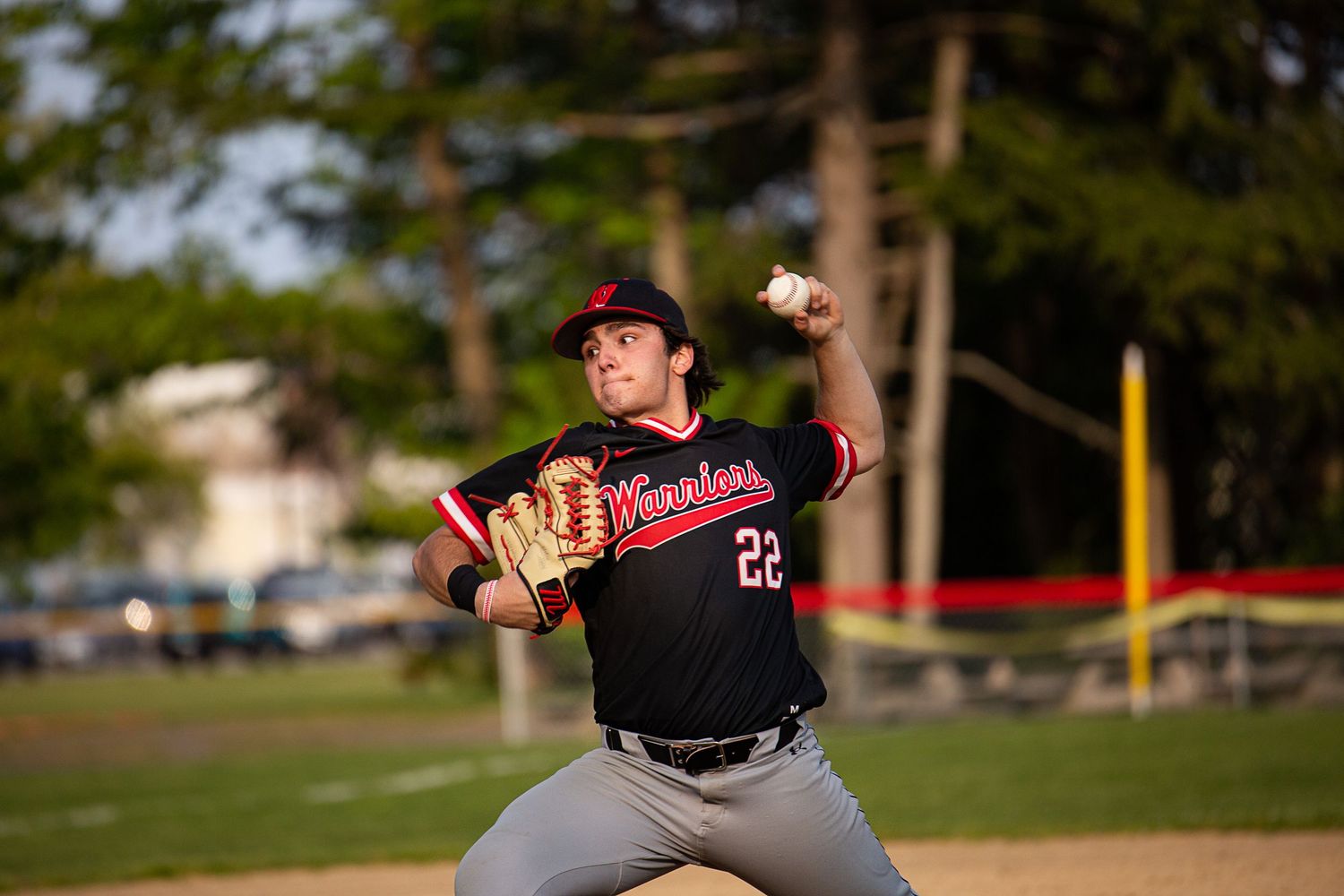 Baseball pitcher in black jersey number 22 winds up to throw during an outdoor game.