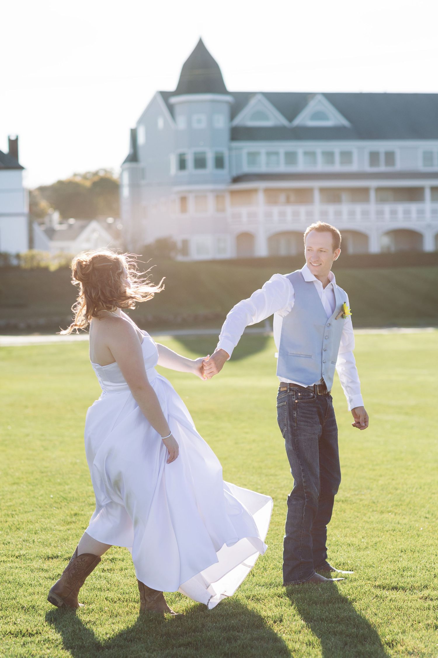 Bride and groom dancing on green lawn with historic white Victorian building in golden sunlight background.