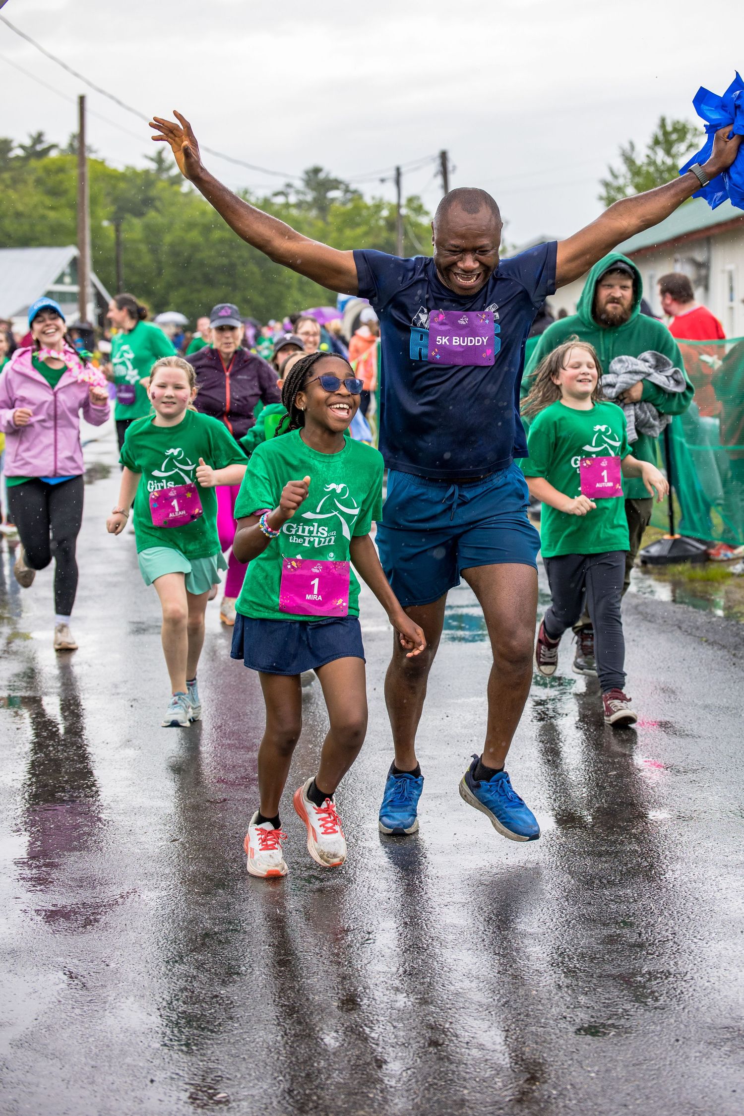Man and girl joyfully crossing finish line at Girls on the Run 5K race on a rainy day.