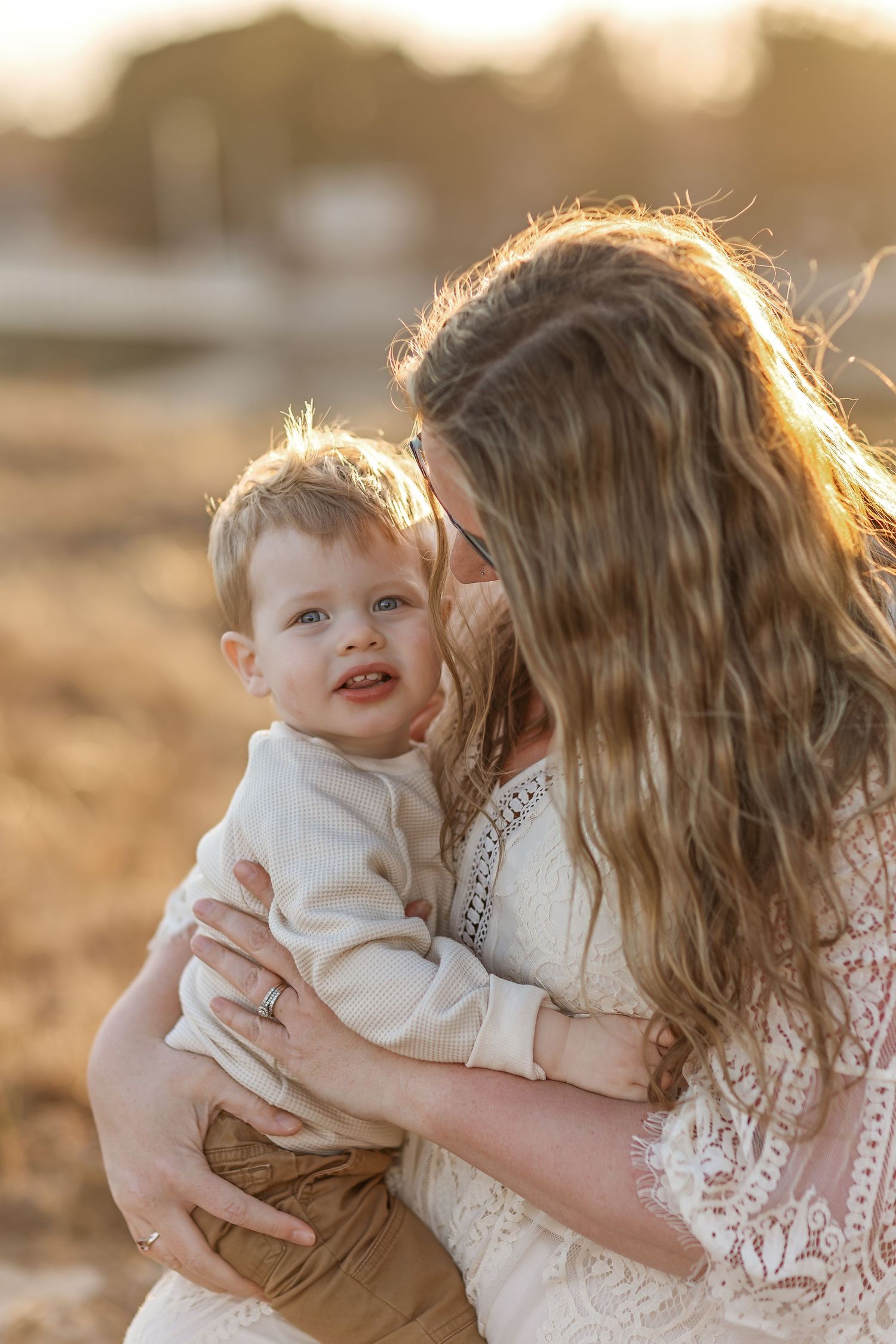 A tender moment captured at golden hour as a baby in white is held lovingly against a warm sunset background.