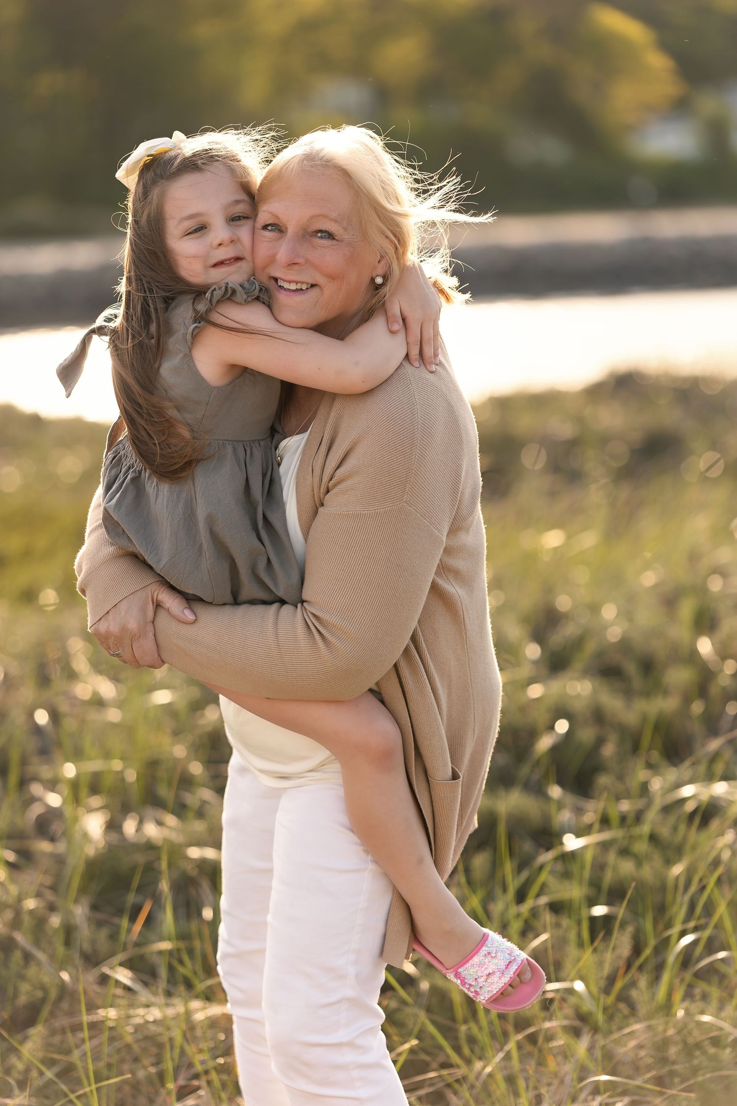 Grandmother holding granddaughter in sunny field, sharing warm hug outdoors in golden light.