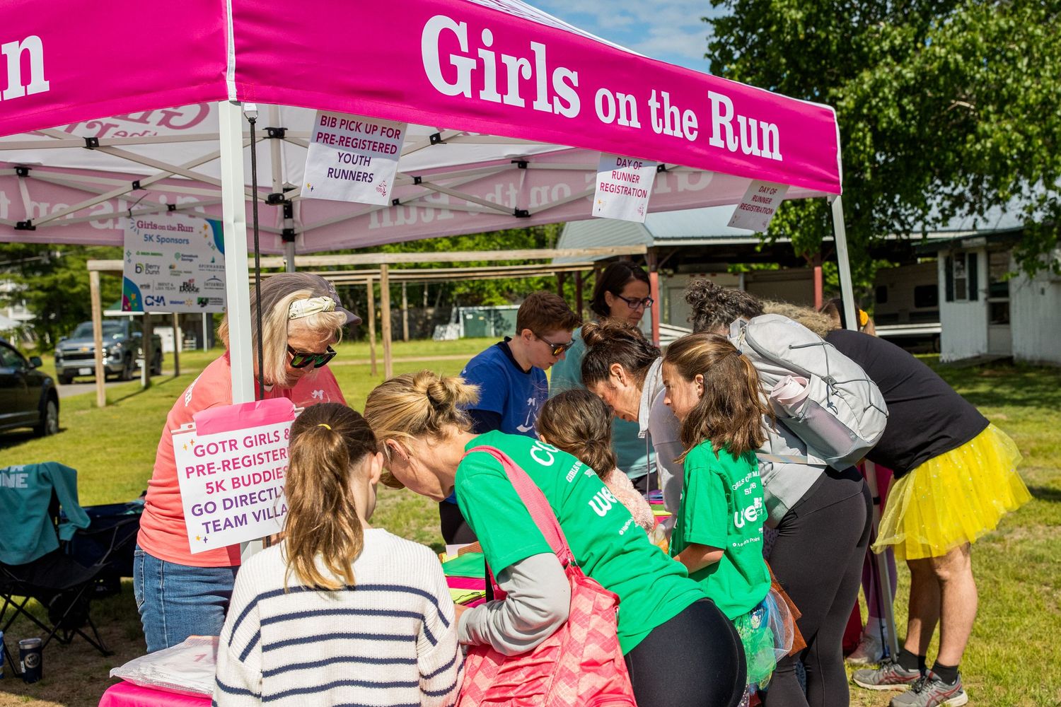 Girls on the Run event with participants gathered under a pink tent at an outdoor registration table.