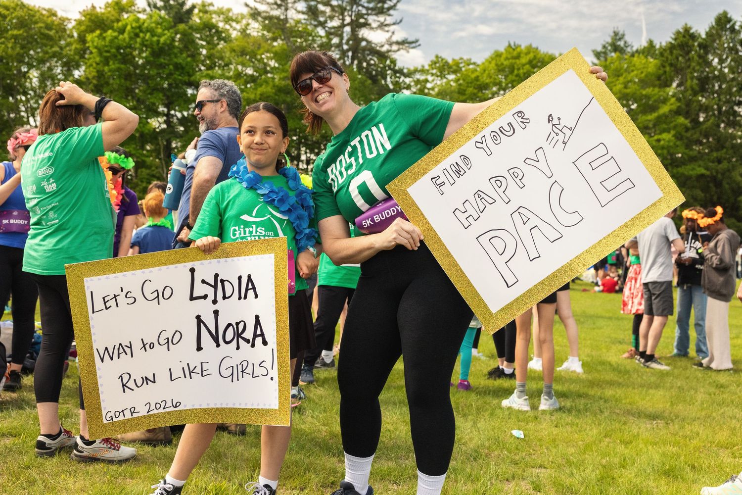Two women holding encouraging race signs at an outdoor running event on a sunny day.