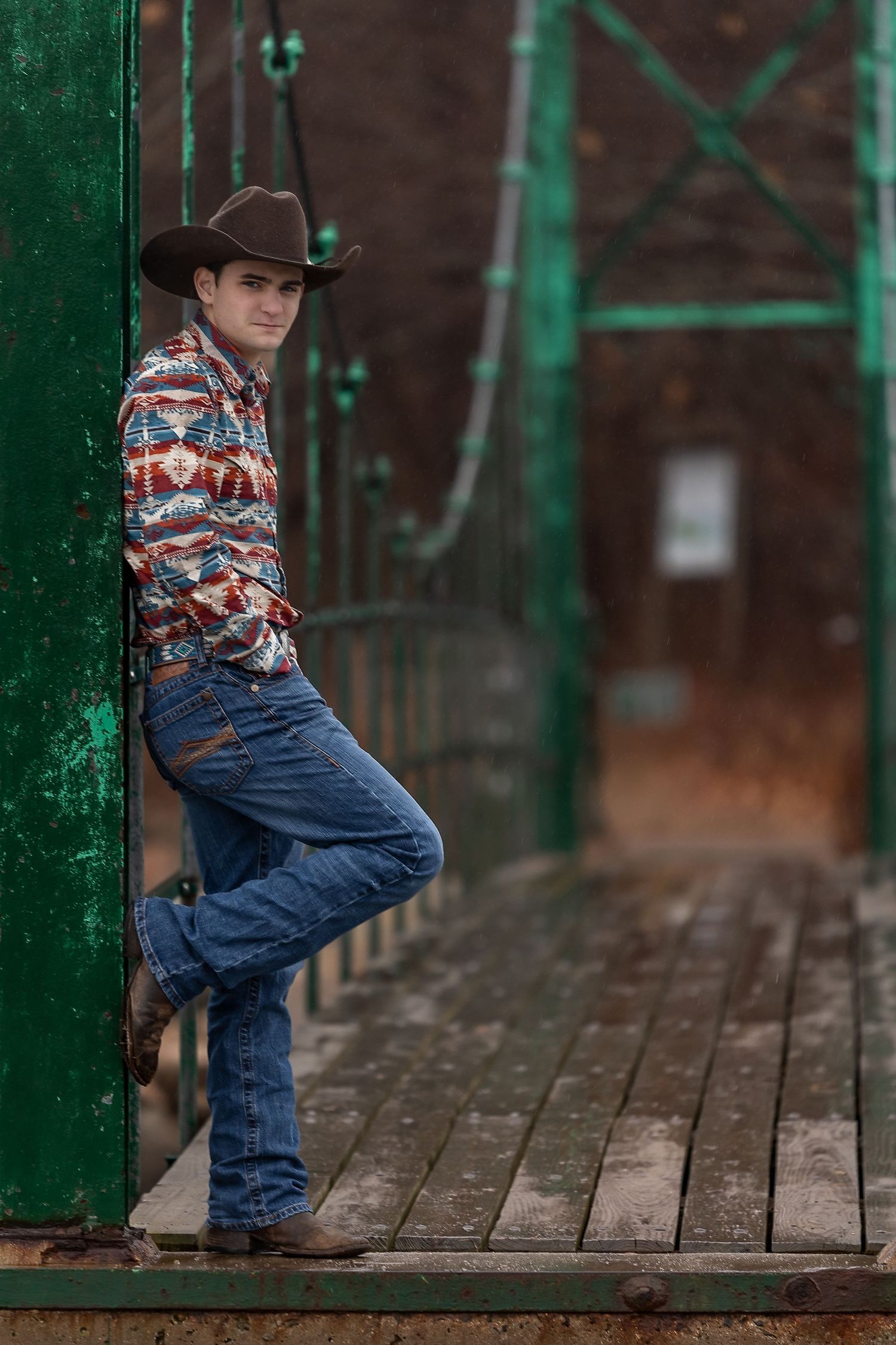 A western-styled photo on a wooden deck with green metal railings featuring cowboy boots, jeans and a patterned shirt.