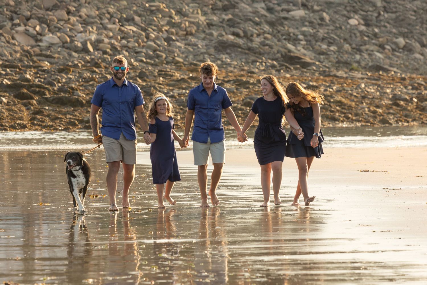 A group walking together with their dog along a reflective beach shoreline at sunset.
