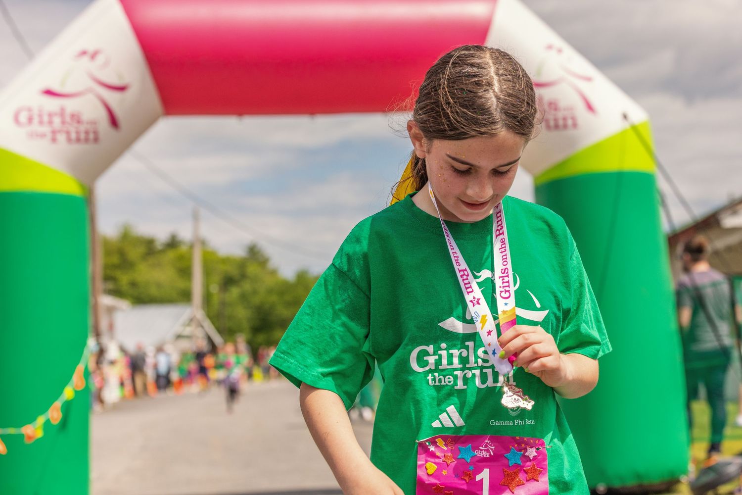 Young girl in green Girls on the Run t-shirt admiring her finisher medal at a 5K race event.