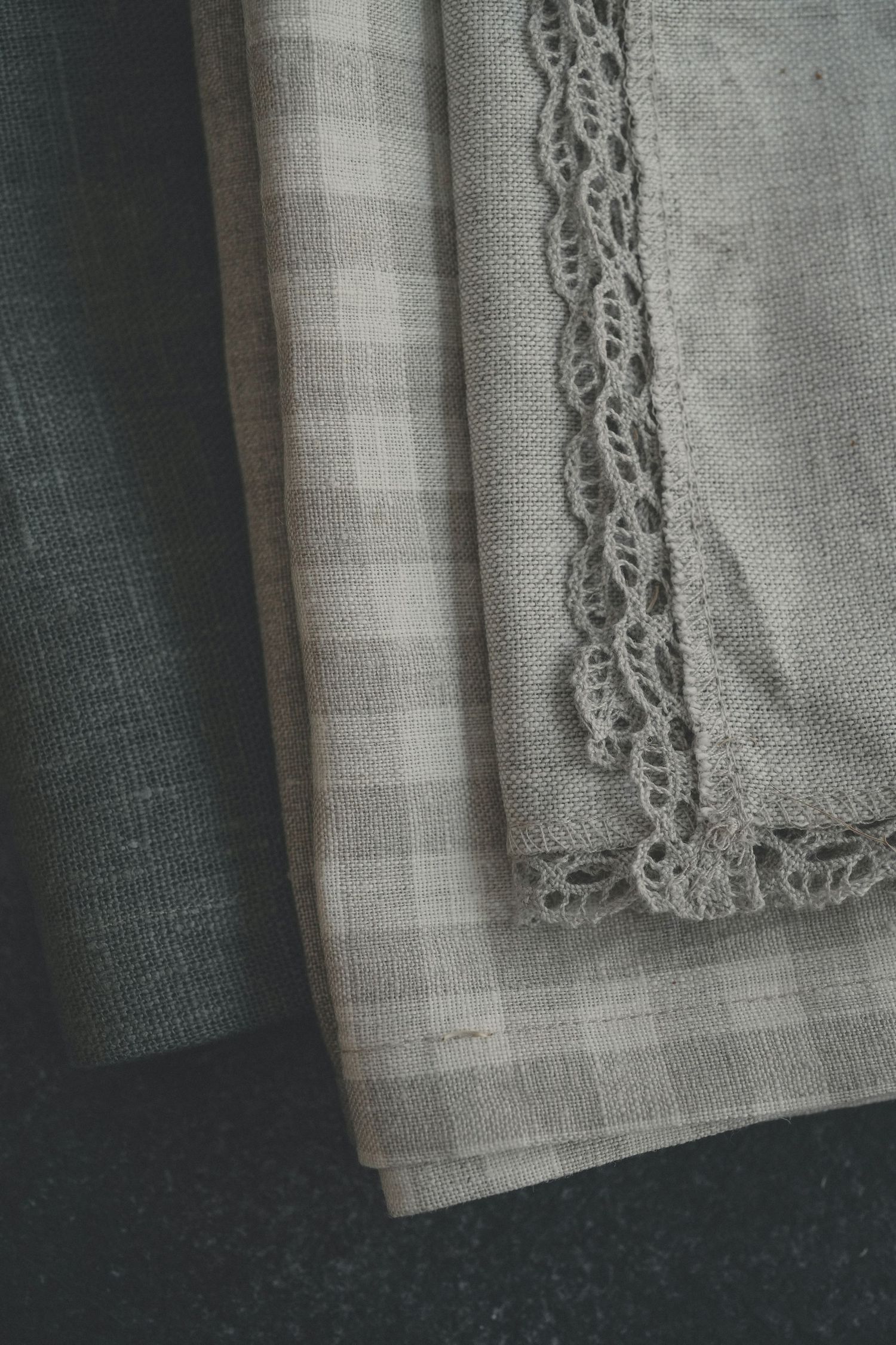 Close-up view of delicate lace trim detail on white linen fabric against a dark background.