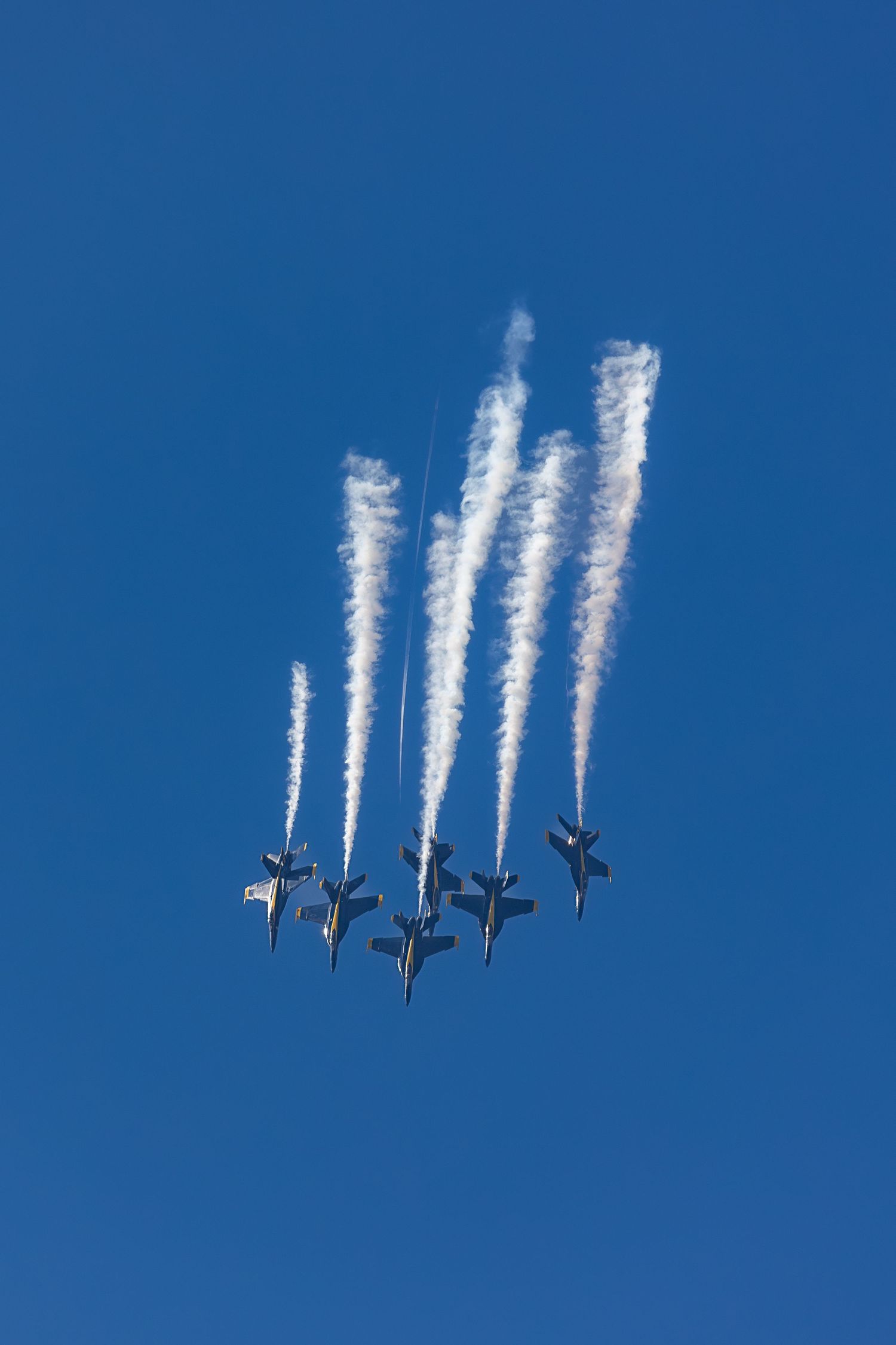 Four military jets performing an aerial formation maneuver against a bright blue sky with white contrails behind them.