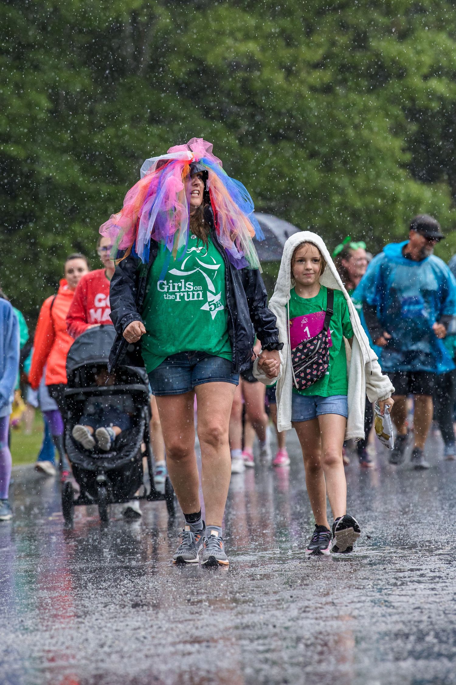 Women and girls walking in heavy rain at a Girls on the Run charity 5K race event, wearing colorful tutus.