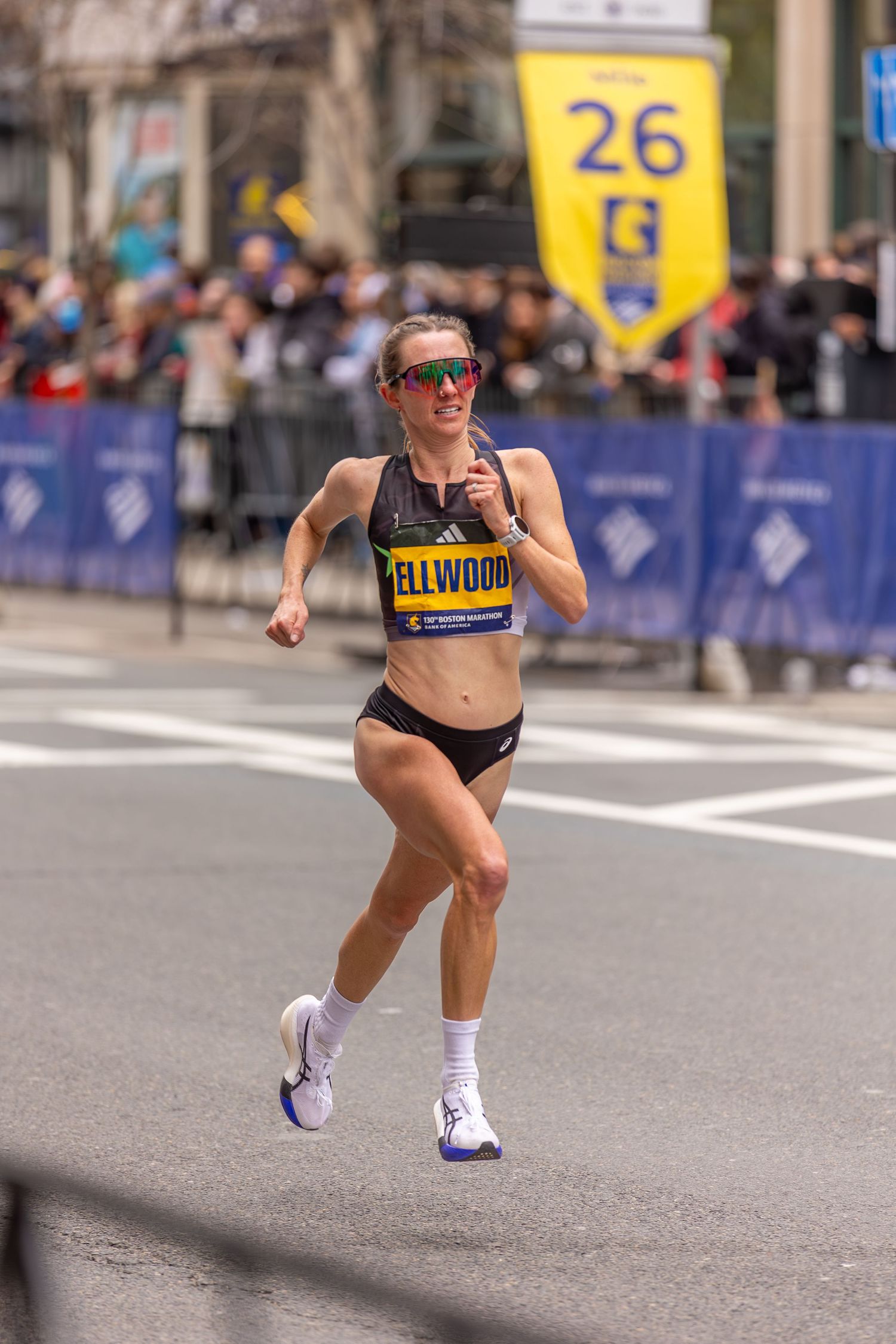 Runner Ellwood competes near mile 26 of the Boston Marathon, wearing sunglasses and race bib on a city street.