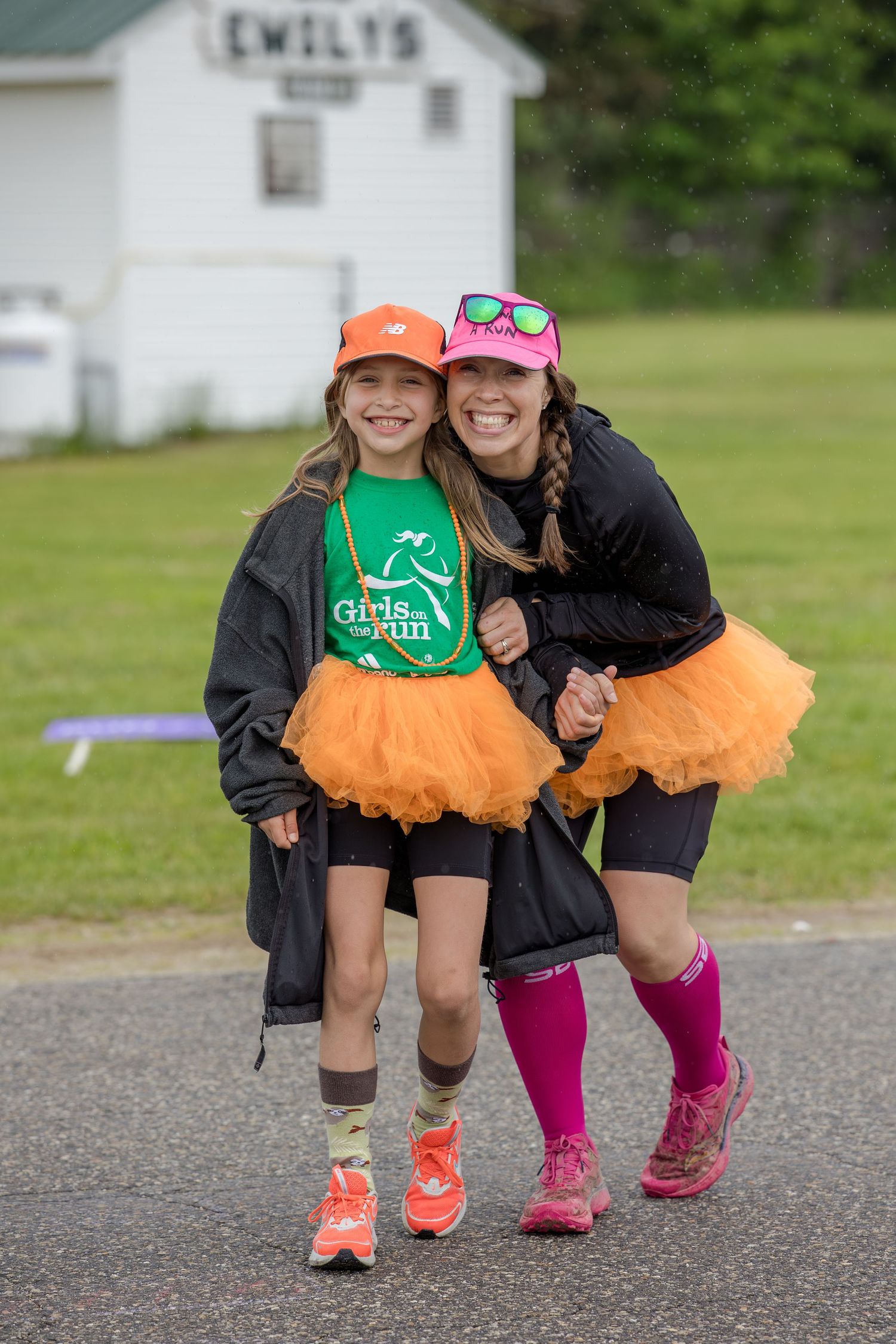 A woman and girl in orange tutus and pink hats pose together at a Girls on the Run charity race event.