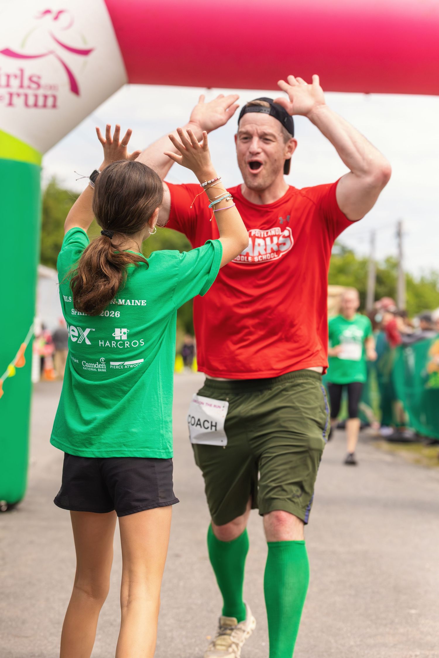 Man in red shirt high-fiving woman in green at Girls on the Run race finish line event.