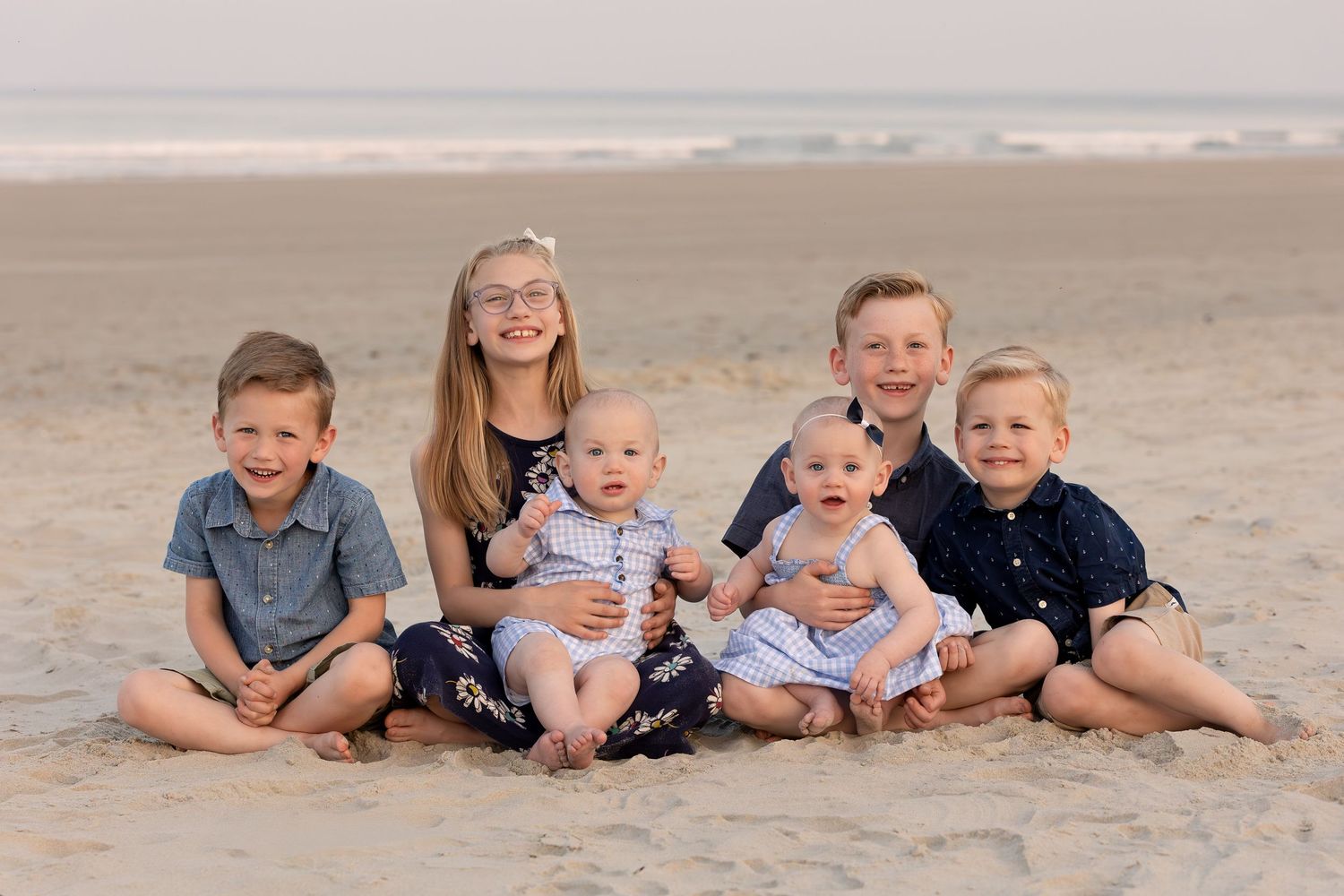 Group of children sitting together on sandy beach during sunset with ocean in background.