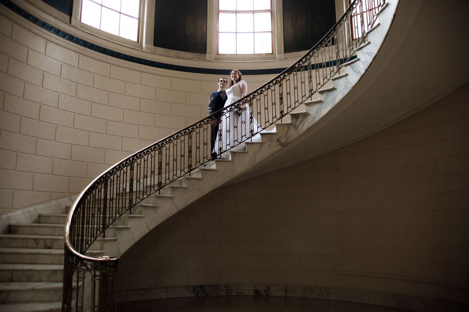 Elegant curved staircase with wrought iron railings and white walls in a historic building interior.