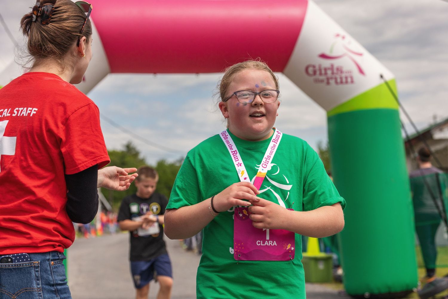 Young girl with Down syndrome smiles after completing a Girls on the Run 5K race, wearing green shirt and medal.