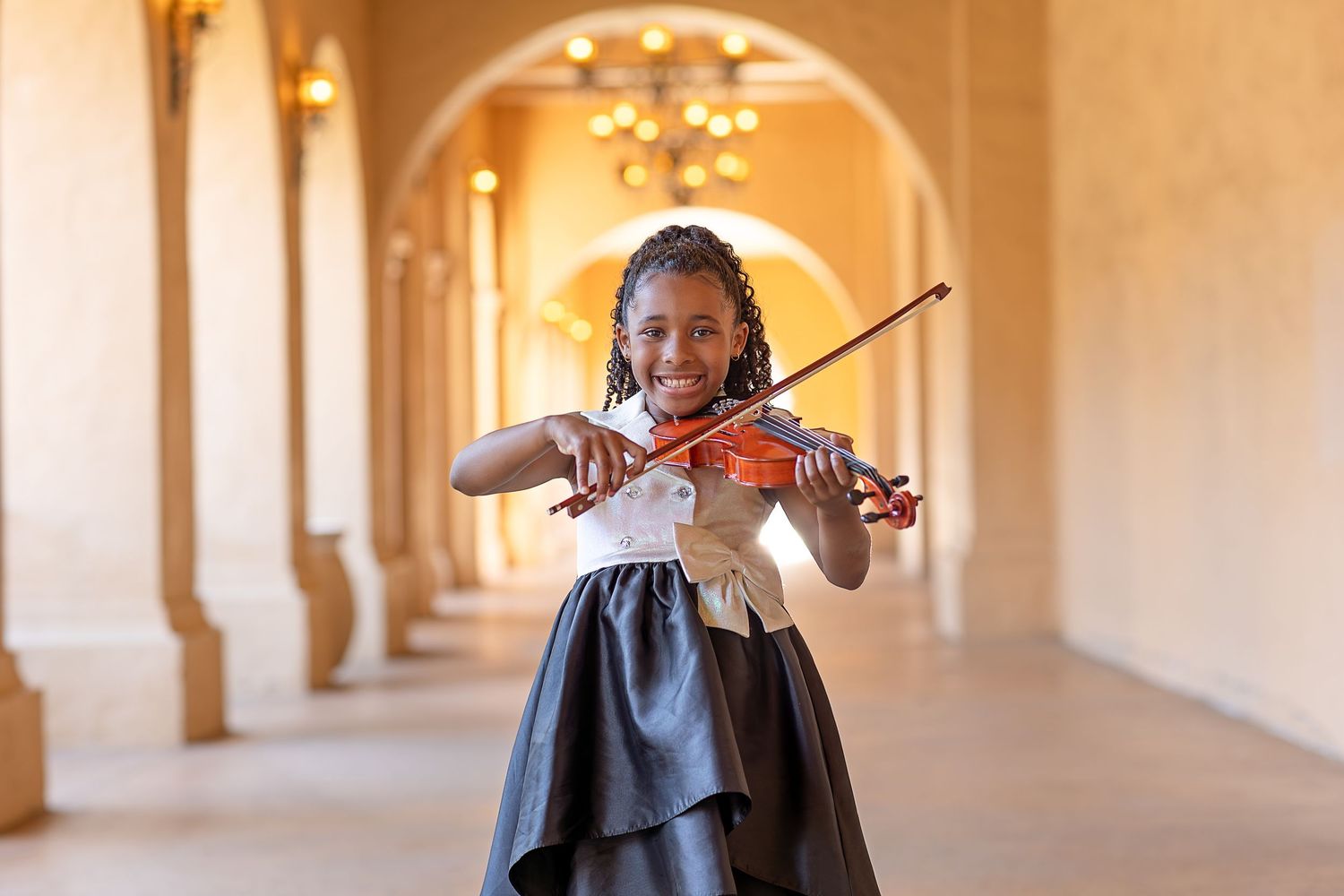 A violinist performs in an elegant arched hallway with warm lighting and classical architectural details.