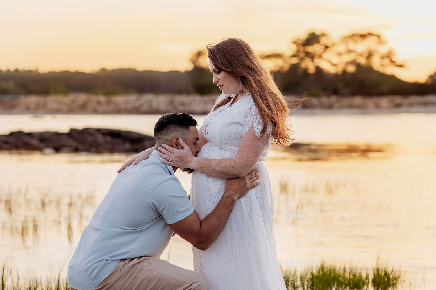 A couple embraces during a romantic sunset maternity photoshoot at Cape Neddick Beach with golden light reflecting off the water.